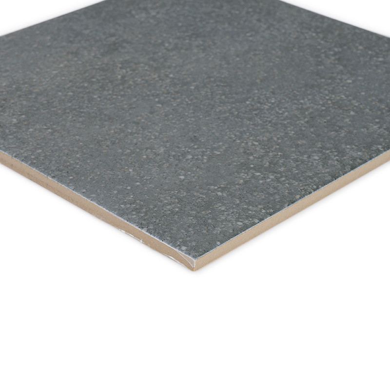A square, gray ceramic tile lies flat, showing a textured, speckled surface with a smooth edge, suitable for flooring or walls.