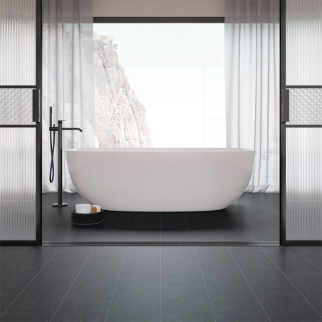 Eine weiße freistehende Badewanne steht in der Mitte eines minimalistischen Badezimmers mit schwarzen Fliesen, eingerahmt von gr