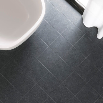 Dunkelgraue quadratische Fliesen bilden ein Gittermuster auf einem Badezimmerboden neben einer weißen Badewanne und einem transp
