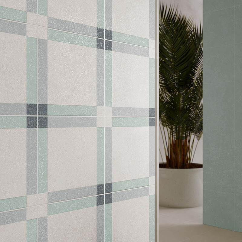 Un mur carrelé présente un motif à carreaux en gris doux, vert et bleu, placé à l'intérieur à côté d'un palmier en pot dans une 