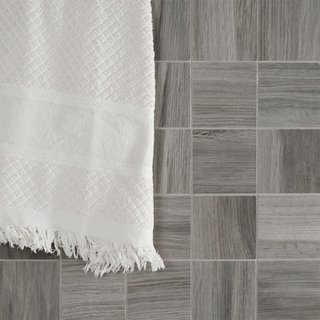 Een witte handdoek met textuur hangt over een raster van kleine, vierkante grijze tegels met een houtachtig patroon, waardoor ee Een witte handdoek met textuur hangt over een raster van kleine, vierkante grijze tegels met een houtachtig patroon, waardoor ee