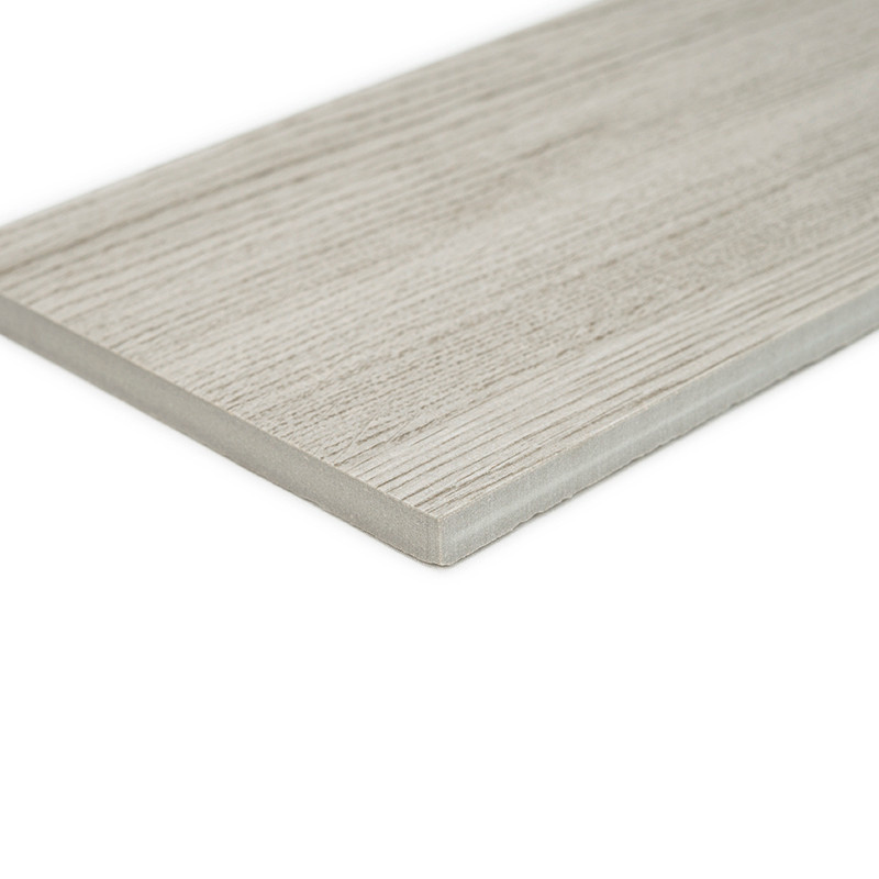 Um ladrilho retangular cinza claro com um padrão de veios de madeira repousa sobre uma superfície branca lisa, exibindo suas bor