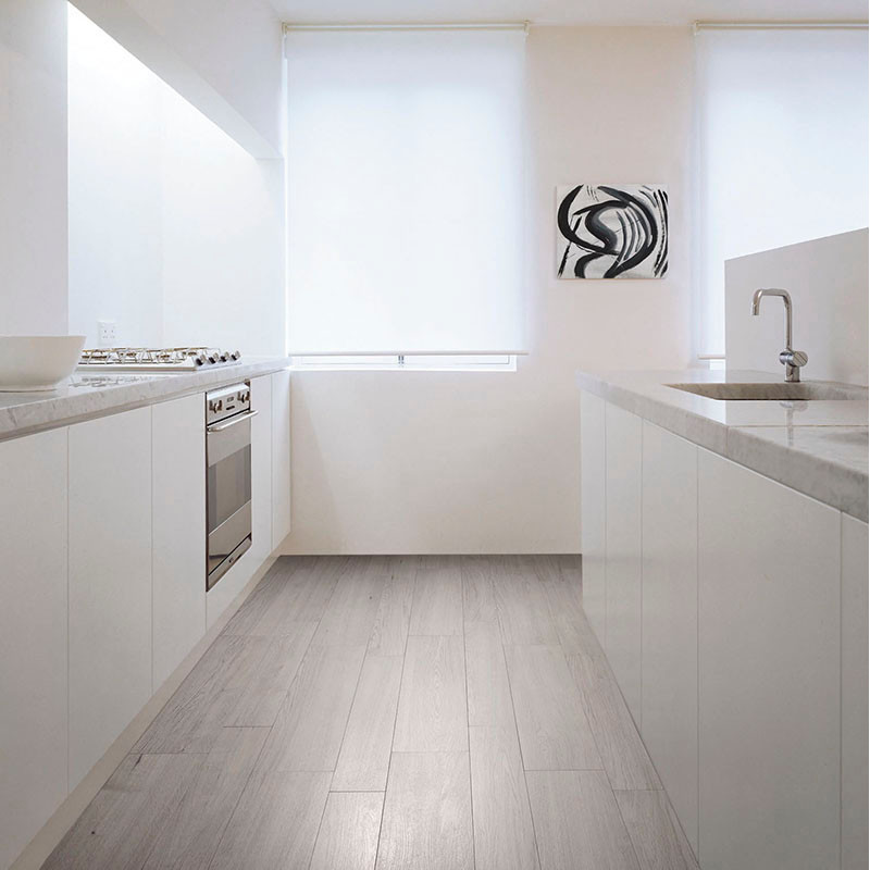 Een moderne keuken is voorzien van strakke witte kasten en werkbladen met een grijze tegelvloer met houtstructuur, onder zacht n