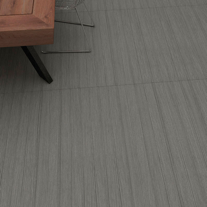 Uma perna de mesa de madeira repousa sobre azulejos cinza texturizados com linhas verticais sutis, situada em um ambiente intern