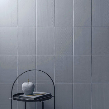 Grijze vierkante tegels bedekken een muur en creëren een gestructureerd oppervlak. Aan de voorkant staat een metalen tafel met e
