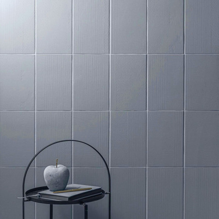 Grijze vierkante tegels bedekken een muur en creëren een gestructureerd oppervlak. Aan de voorkant staat een metalen tafel met e Grijze vierkante tegels bedekken een muur en creëren een gestructureerd oppervlak. Aan de voorkant staat een metalen tafel met e
