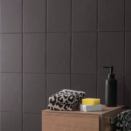 Ladrilhos de textura escura cobrem uma parede. Sobre uma superfície de madeira, toalhas com estampa de leopardo ficam ao lado de