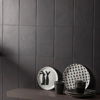 Dunkle, strukturierte Fliesen bilden eine moderne Wand. Auf einem Holzregal stehen Teller mit minimalistischen Hasen- und Dreiec