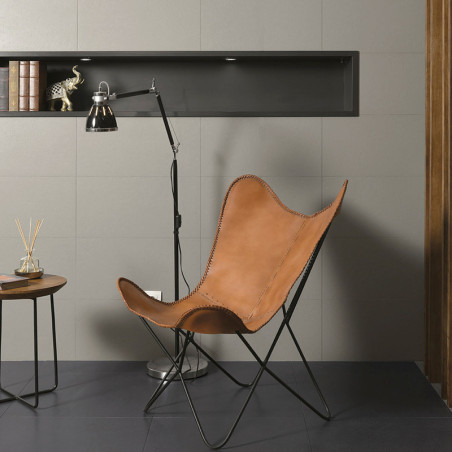 Uma cadeira borboleta de couro fica no piso de cerâmica escura, ao lado de uma luminária de chão moderna e uma pequena mesa redo Uma cadeira borboleta de couro fica no piso de cerâmica escura, ao lado de uma luminária de chão moderna e uma pequena mesa redo