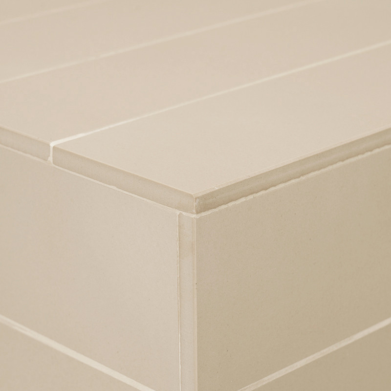Azulejo retangular bege com superfície lisa formando parte de um padrão estruturado em camadas em um ambiente minimalista.