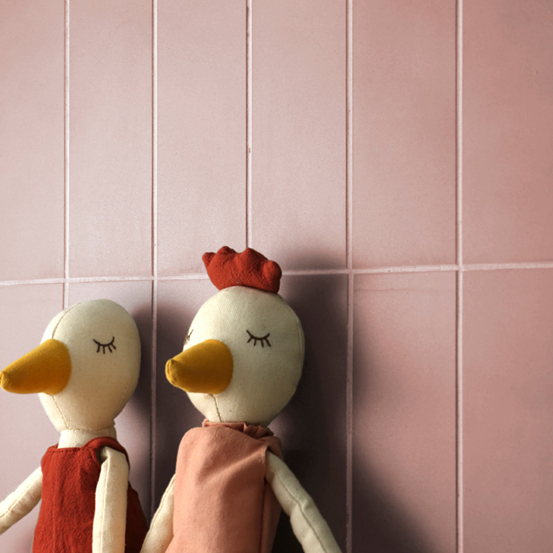 Twee pluche eendfiguren staan ​​leunend tegen een roze betegelde muur, beiden met gesloten ogen en gekleed in rode en roze outfi