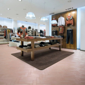 A wooden table displays folded clothes on a brown rug in a modern retail store, surrounded by hanging apparel and soft lighting.