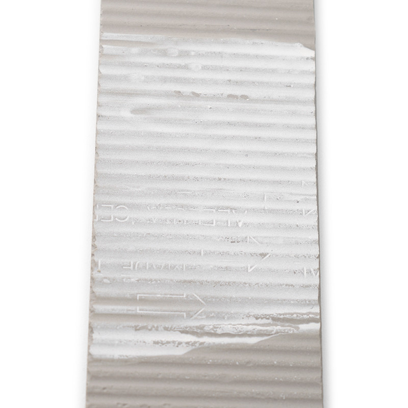 Die rechteckige Kachel zeigt horizontale Rippen mit teilweisem Text mit der Aufschrift „MADE IN“ und Richtungspfeilen vor einem 