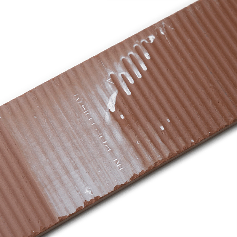 A rectangular, ribbed, brown ceramic tile with a glossy white streak diagonally across it. Embossed text reads `IN AXIMUS` along