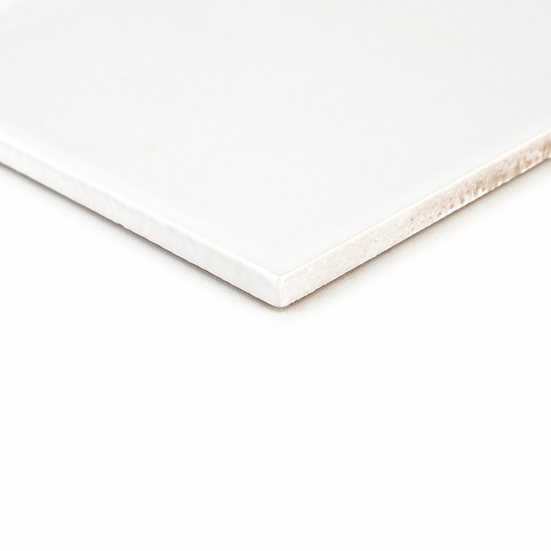 A white ceramic tile with smooth edges lies on a plain, light background, highlighting its glossy surface and thickness.