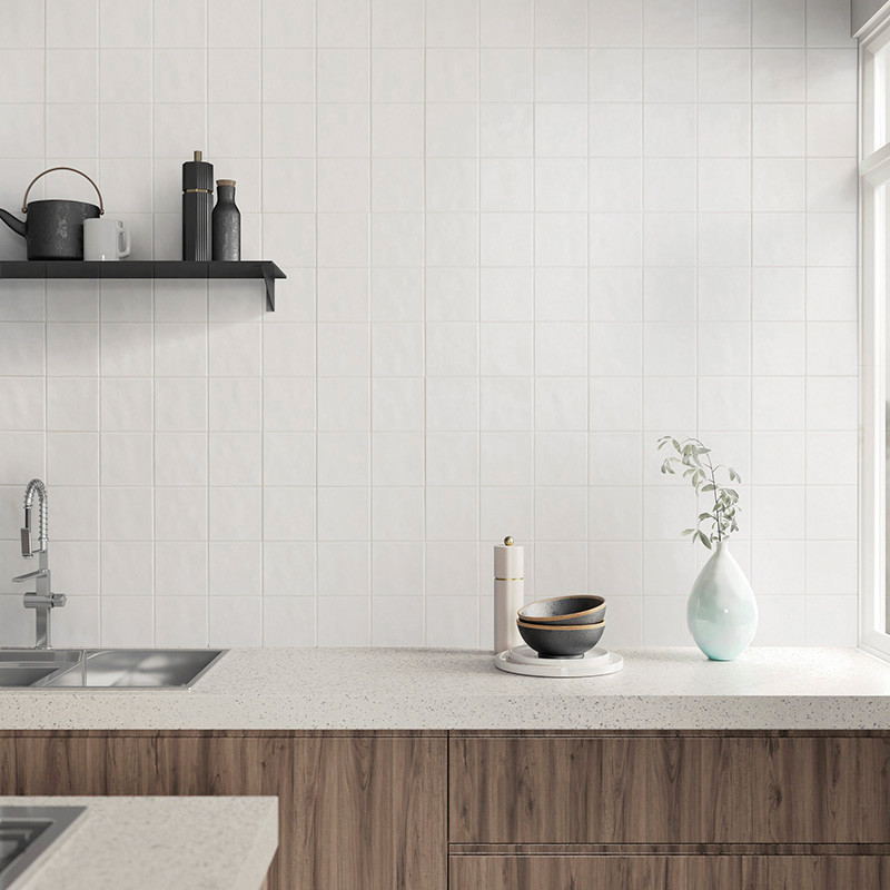 Uma cozinha moderna apresenta azulejos quadrados brancos como backsplash. Uma bancada contém uma tigela, uma xícara e um vaso. u