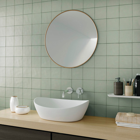 Een witte ovale gootsteen staat op een houten aanrecht onder een grote ronde spiegel, omgeven door groene tegels, toiletartikele Een witte ovale gootsteen staat op een houten aanrecht onder een grote ronde spiegel, omgeven door groene tegels, toiletartikele