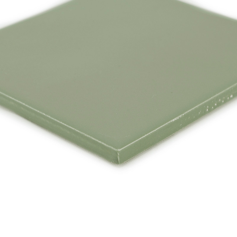 Un carreau vert carré et lisse repose sur une surface blanche, affichant un éclat subtil avec des bords légèrement arrondis et a