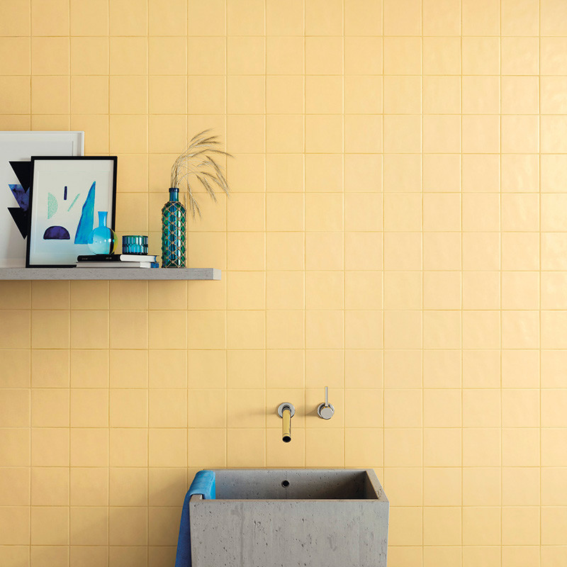 Uma parede de azulejos amarelo fosco apresenta uma pia minimalista de concreto com uma toalha azul, colocada abaixo de uma prate