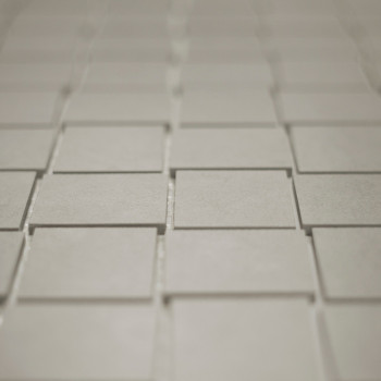 Vierkante tegels zijn gerangschikt in een verspringend rasterpatroon, waardoor een subtiel driedimensionaal effect ontstaat. De 