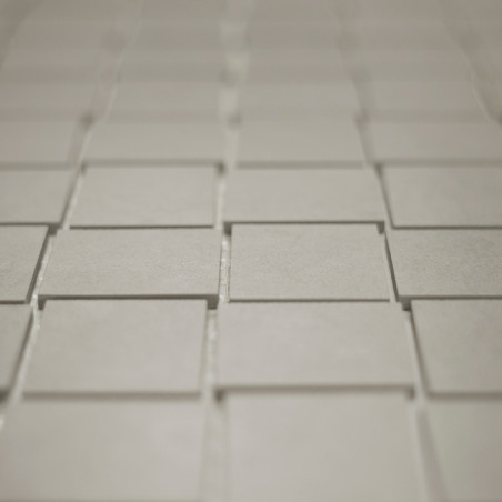 Vierkante tegels zijn gerangschikt in een verspringend rasterpatroon, waardoor een subtiel driedimensionaal effect ontstaat. De 