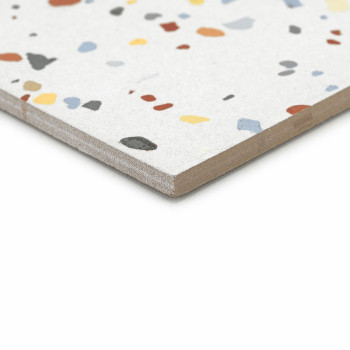 A terrazzo tile lies flat, displaying colorful, irregular stone fragments on a light gray surface, with a smooth, beveled edge.
