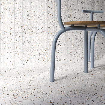 A chair with light blue metal legs stands on a speckled terrazzo floor, against a matching wall, creating a seamless, modern aes
