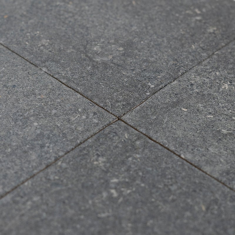 Cuatro azulejos de piedra gris se unen en un punto central, formando un patrón cruzado, con motas sutiles y una superficie textu