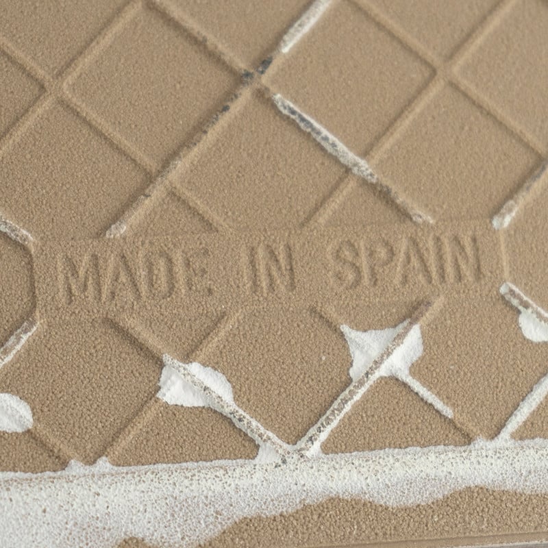 Los azulejos de cerámica beige presentan el texto en relieve `MADE IN SPAIN`, que muestra un patrón de rombos con manchas blanca