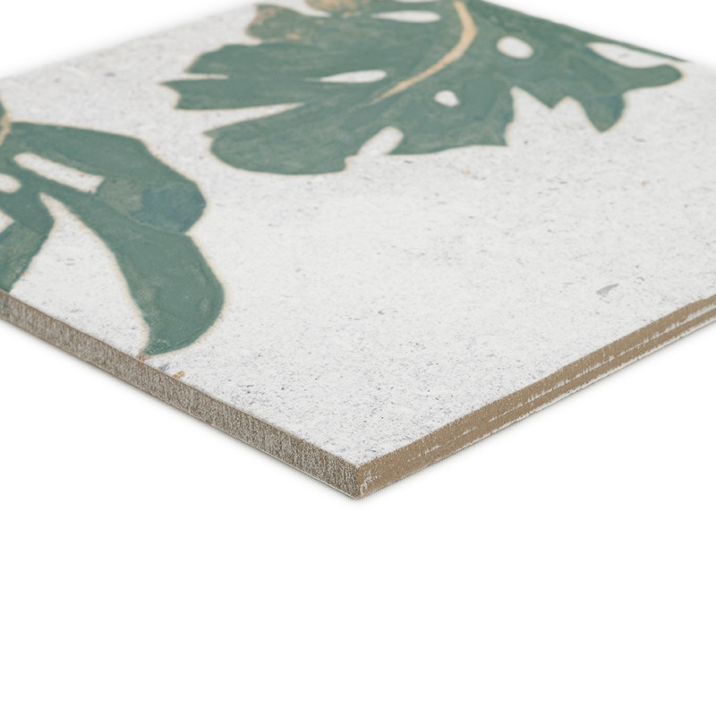 A ceramic tile displays a green leaf motif on a white background. Its edge is slightly beveled, highlighting thickness and textu