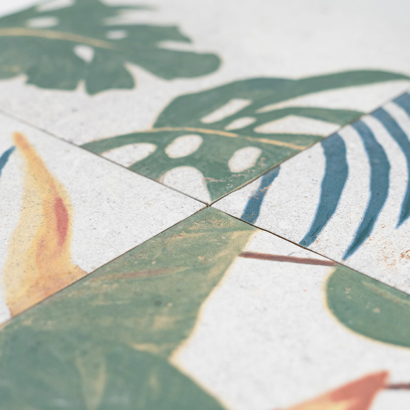 Ceramic tiles feature tropical leaf designs, primarily green with hints of yellow and blue. The tiles are arranged in a grid pat