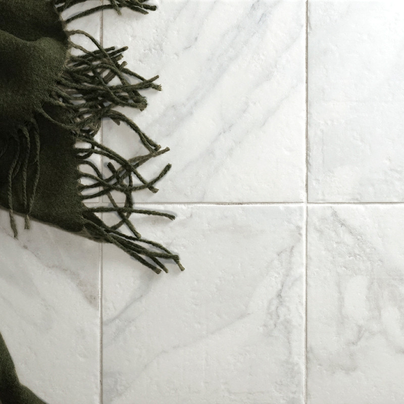 Um tecido com franjas escuras cobre quatro azulejos claros com padrão de mármore, criando um contraste de textura e cor em um am