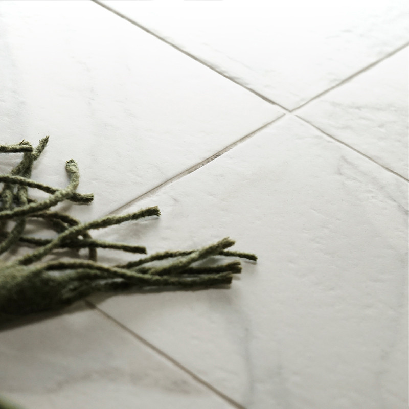 Ladrilhos de mármore branco estão estendidos no chão, com franjas verdes de um tapete próximo cobrindo-os parcialmente.