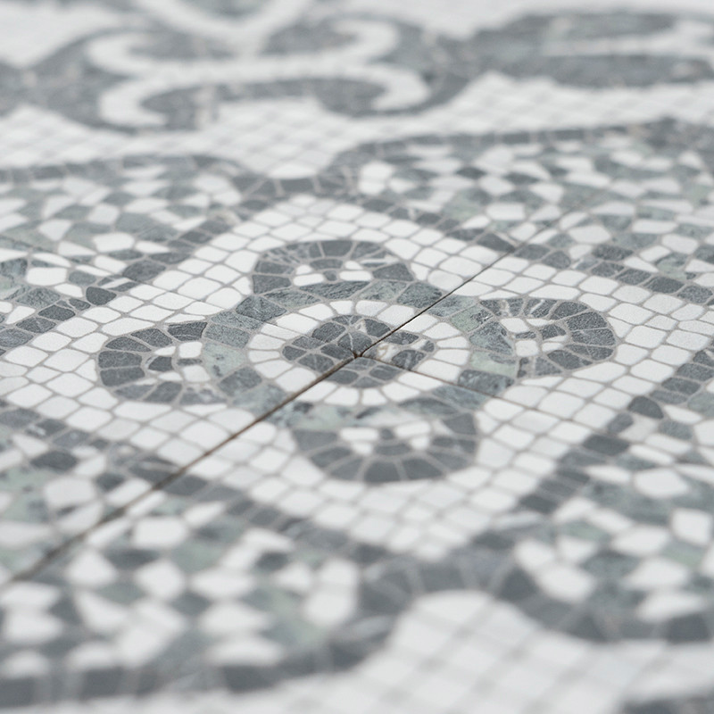 Los mosaicos grises y blancos forman patrones geométricos intrincados, resaltando formas circulares y de diamantes. Los azulejos