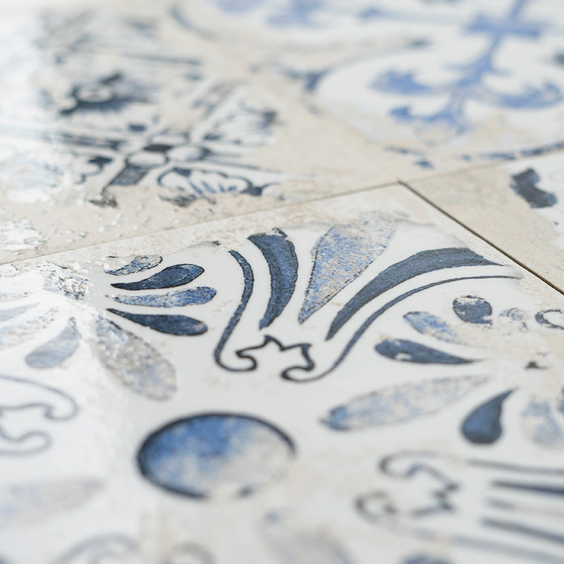 A ceramic tile displays intricate blue floral and geometric patterns, arranged symmetrically, set against a white background, cr