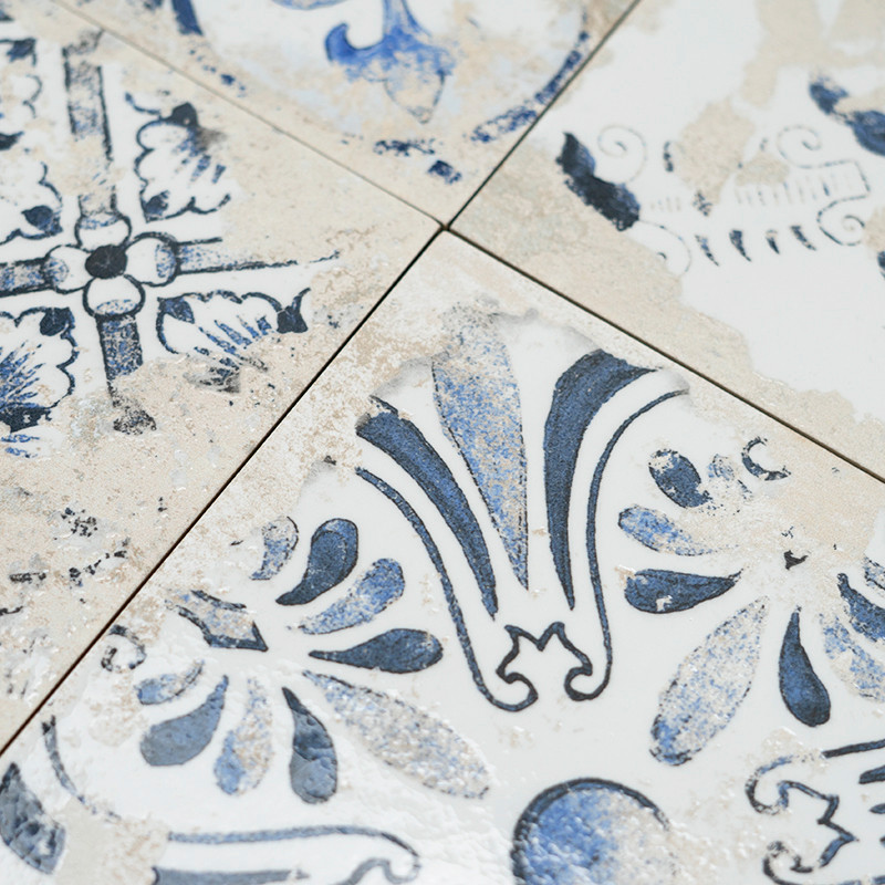 Tiles display intricate blue floral patterns with a weathered look. They intersect at clean lines, creating a vintage and rustic