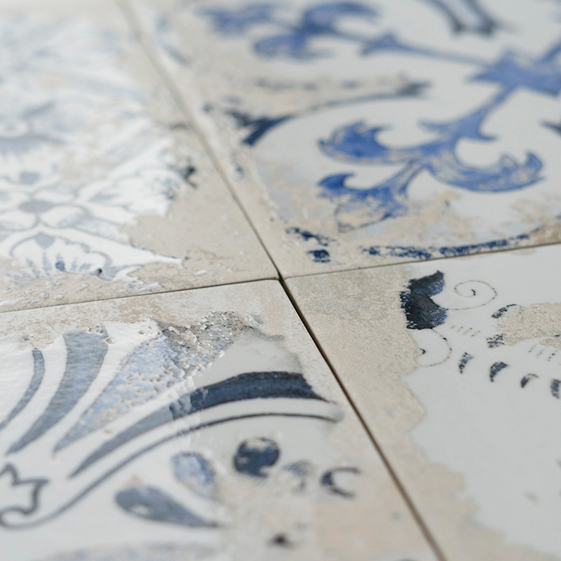 Four ceramic tiles display blue and white floral patterns with a weathered appearance. The close-up shows cracks and fading colo