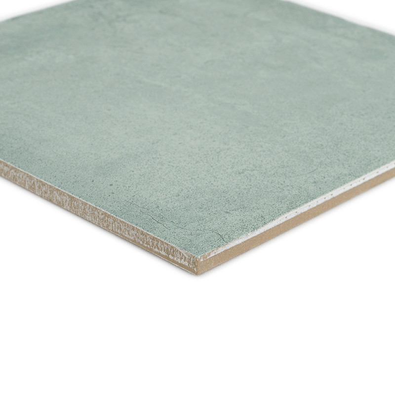 Un carreau de céramique carré vert repose sur une surface blanche, présentant une texture lisse et des bords légèrement biseauté