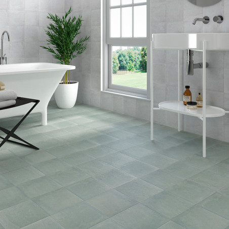 Een badkamer is voorzien van matgrijze tegels op de vloer, een vrijstaand wit bad, een moderne wastafel en een hoge potplant bij Een badkamer is voorzien van matgrijze tegels op de vloer, een vrijstaand wit bad, een moderne wastafel en een hoge potplant bij