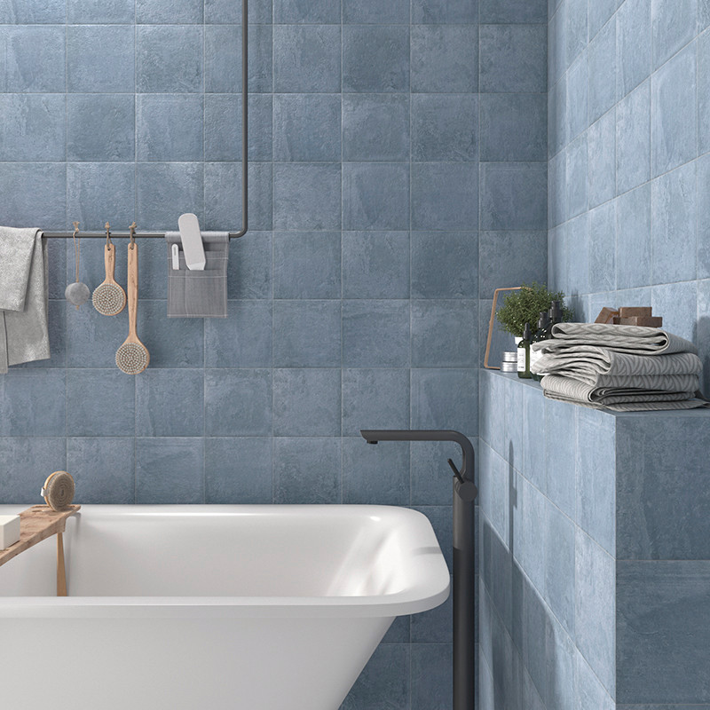 Ceramic tiles cover bathroom walls, creating a calming blue ambiance. A bathtub, shelves with folded towels, and toiletries comp