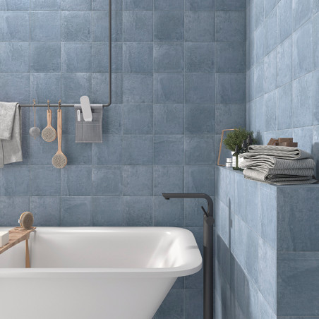 Ceramic tiles cover bathroom walls, creating a calming blue ambiance. A bathtub, shelves with folded towels, and toiletries comp