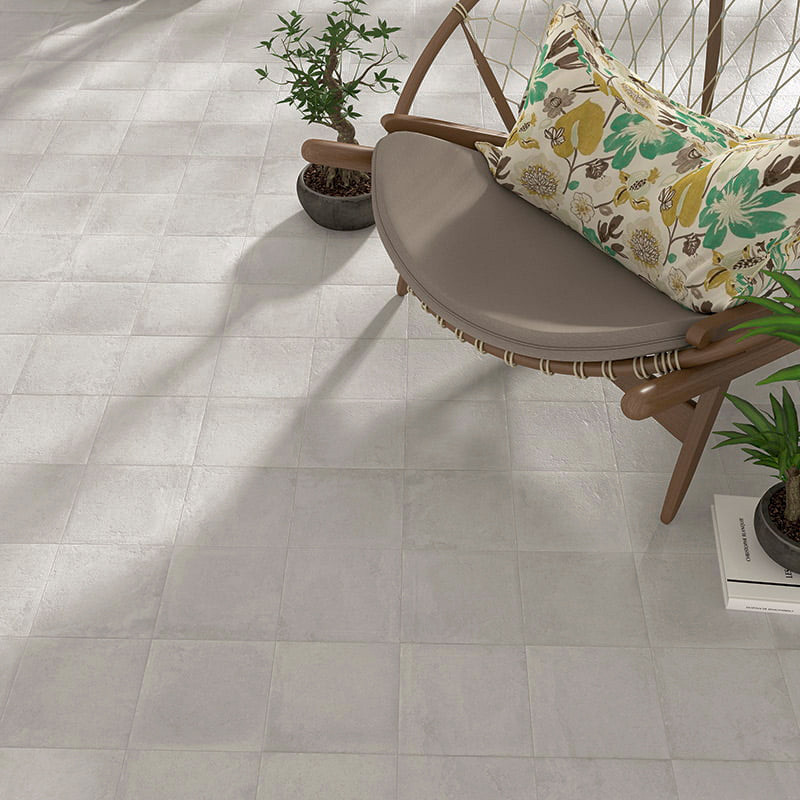 Horizontaal is een beige mozaïektegelvloer gelegd, grenzend aan een moderne, ronde stoel met bloemenkussen, omgeven door potplan