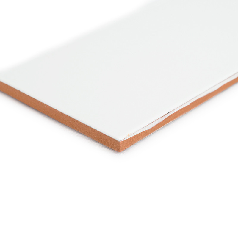 A rectangular tile with a glossy white surface sits against a white background, revealing an exposed brown edge at the corner.