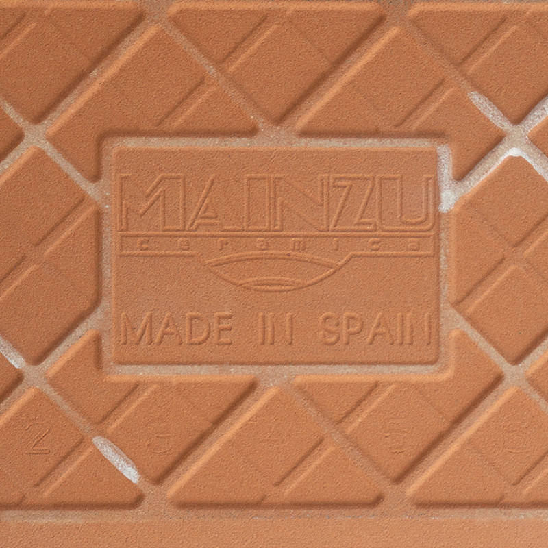 Um ladrilho cerâmico de terracota apresenta padrões de diamante em relevo e texto em relevo que diz “MAINZU ceramica” e “MADE IN
