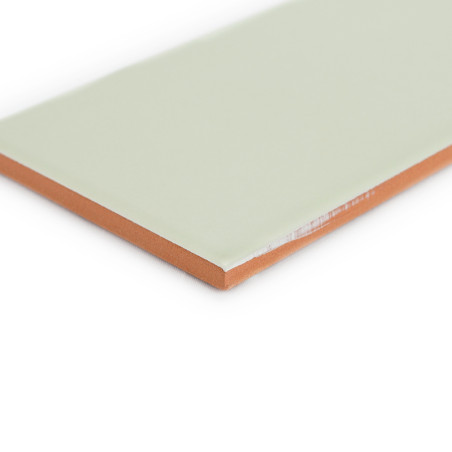 Eine rechteckige Fliese mit einer glatten, blassgrünen Oberfläche liegt flach liegend mit sichtbaren orangebraunen Kanten in ein Eine rechteckige Fliese mit einer glatten, blassgrünen Oberfläche liegt flach liegend mit sichtbaren orangebraunen Kanten in ein