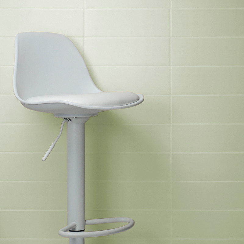 Un tabouret de bar pivotant blanc se dresse contre un mur carrelé vert clair, avec son levier visible, évoquant un cadre épuré e