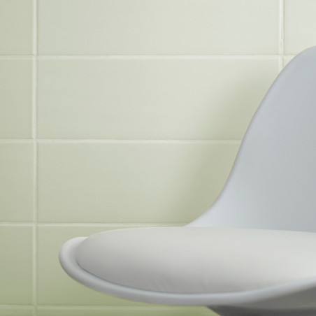 Ein moderner, geschwungener weißer Stuhl steht an einer Wand aus glatten, hellgrünen Fliesen und schafft eine minimalistische In Ein moderner, geschwungener weißer Stuhl steht an einer Wand aus glatten, hellgrünen Fliesen und schafft eine minimalistische In