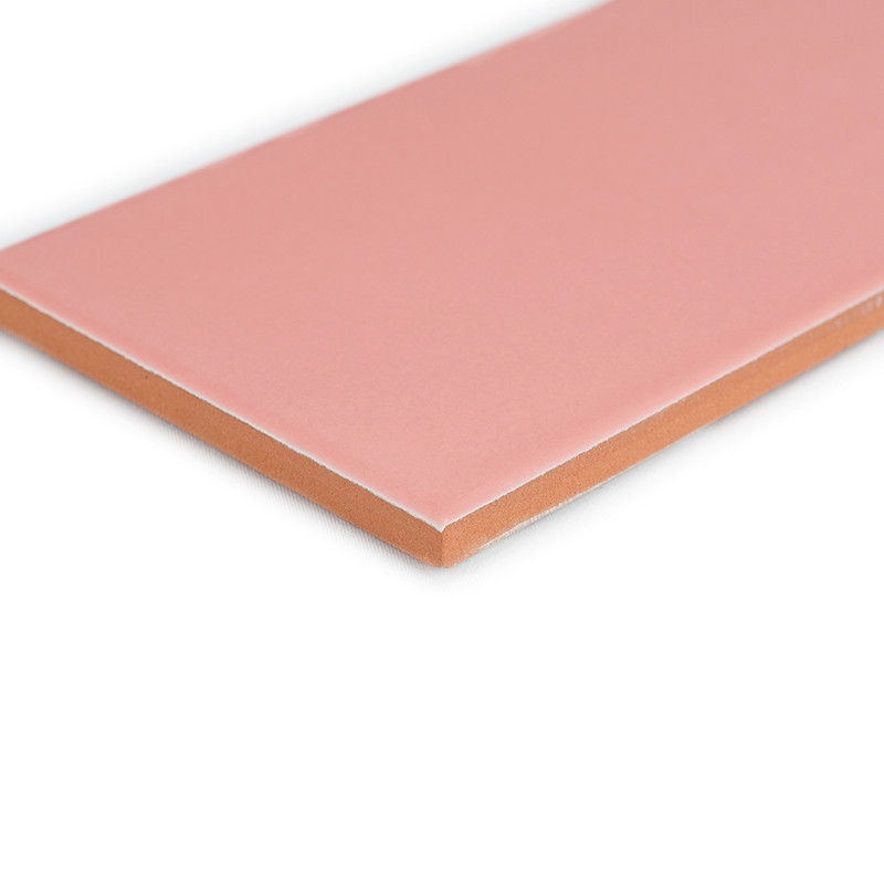 Un azulejo rosa rectangular, liso, descansa sobre un fondo blanco, resaltando sus bordes limpios y su parte inferior de color te