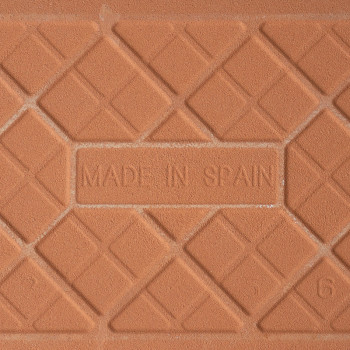 Un carreau en terre cuite comporte le texte en relief « MADE IN SPAIN » entouré d'un motif géométrique de lignes diagonales qui 
