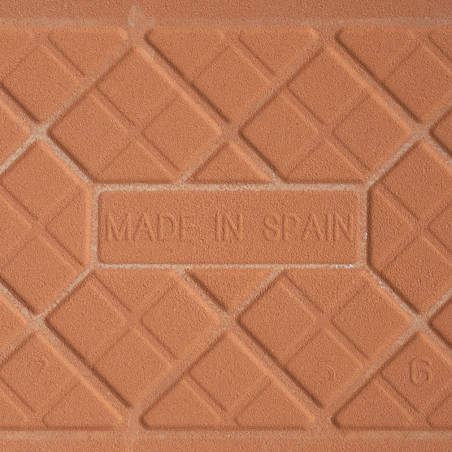 Un carreau en terre cuite comporte le texte en relief « MADE IN SPAIN » entouré d'un motif géométrique de lignes diagonales qui  Un carreau en terre cuite comporte le texte en relief « MADE IN SPAIN » entouré d'un motif géométrique de lignes diagonales qui